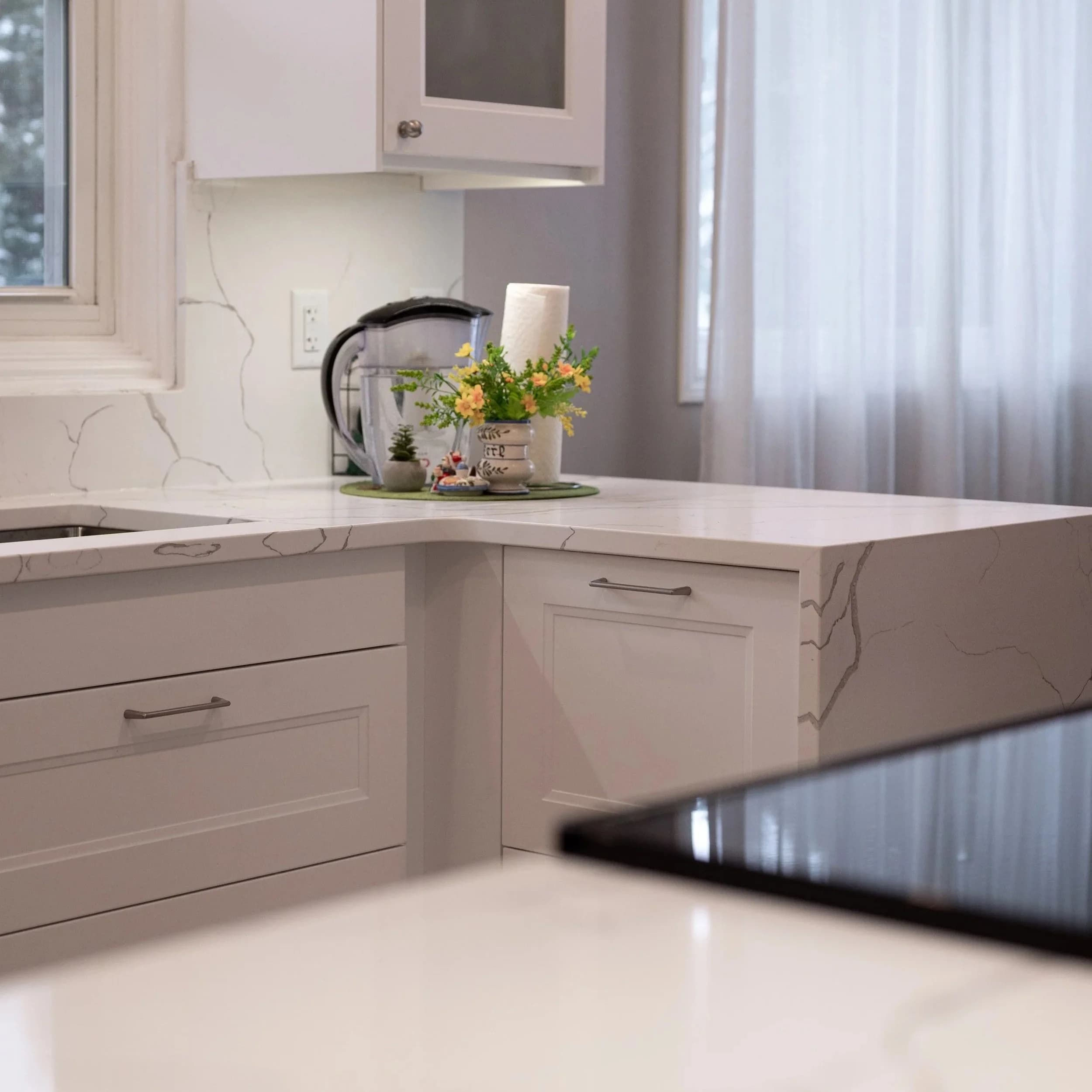 Kitchen with white quartz waterfall countertop, grey shaker cabinets, and white veined backsplash.